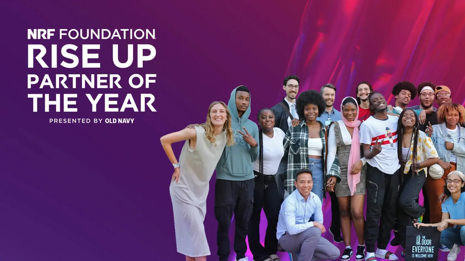 Teachers and students representing the RISE UP Partner of the Year: The Door. Located in NYC, the image's people are of various ages and backgrounds. They are smiling together in front of a vibrant purple and red gradient backdrop. One person holds a totebag that reads The Door: Everyone is Welcome Here. In the upper-left, text added to the iamge says NRF Foundation Rise Up Partner of the Year presented by Old Navy.